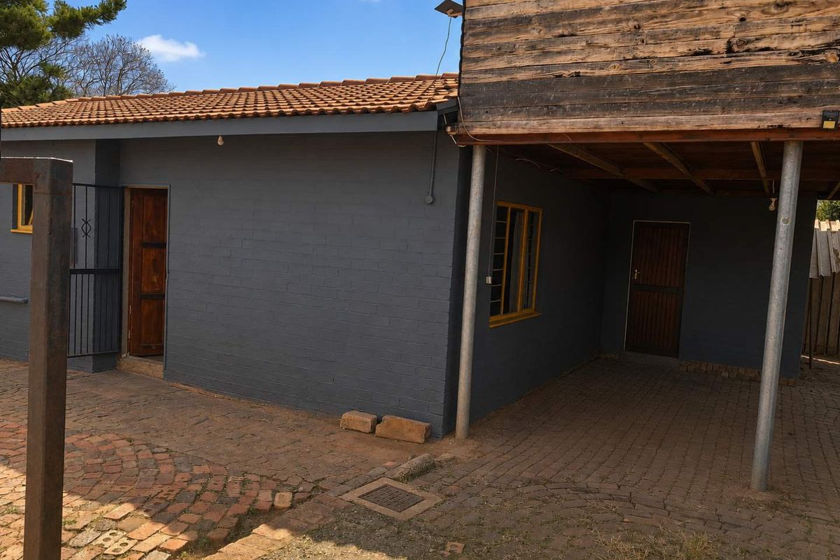 Rear exterior view of the property featuring a paved courtyard area, brick walls, and a raised timber-clad structure supported by steel columns.