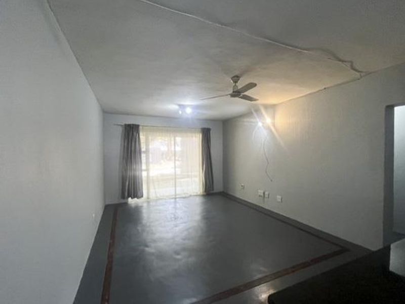 An empty living room featuring a ceiling fan, painted concrete flooring, and a sliding glass door providing natural light.