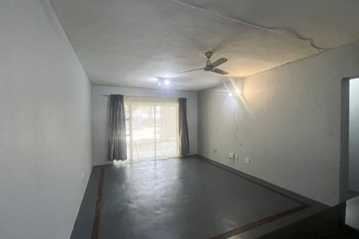 An empty living room featuring a ceiling fan, painted concrete flooring, and a sliding glass door providing natural light.