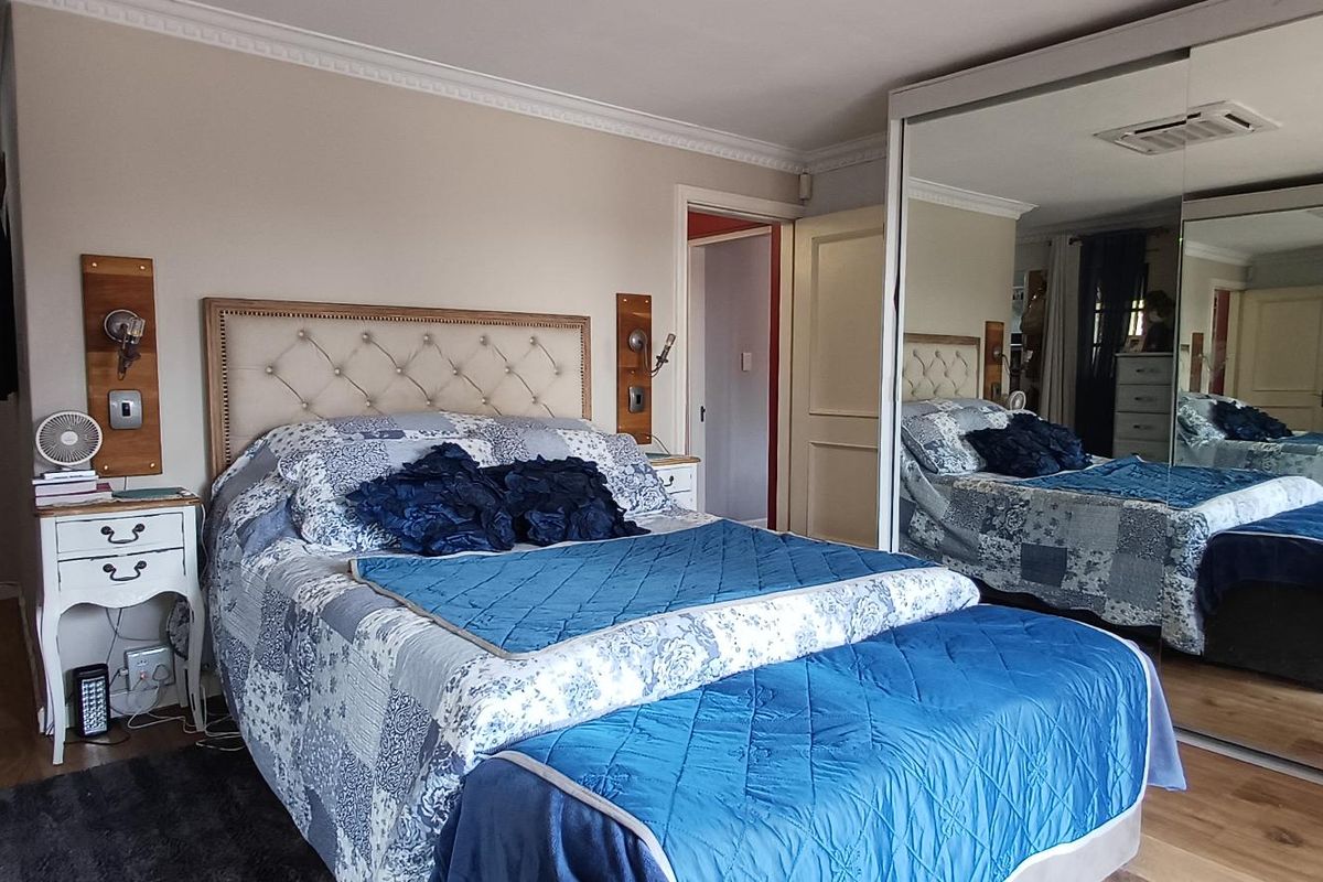 A well-maintained bedroom featuring laminate flooring, crown molding, and a large built-in wardrobe with mirrored sliding doors.