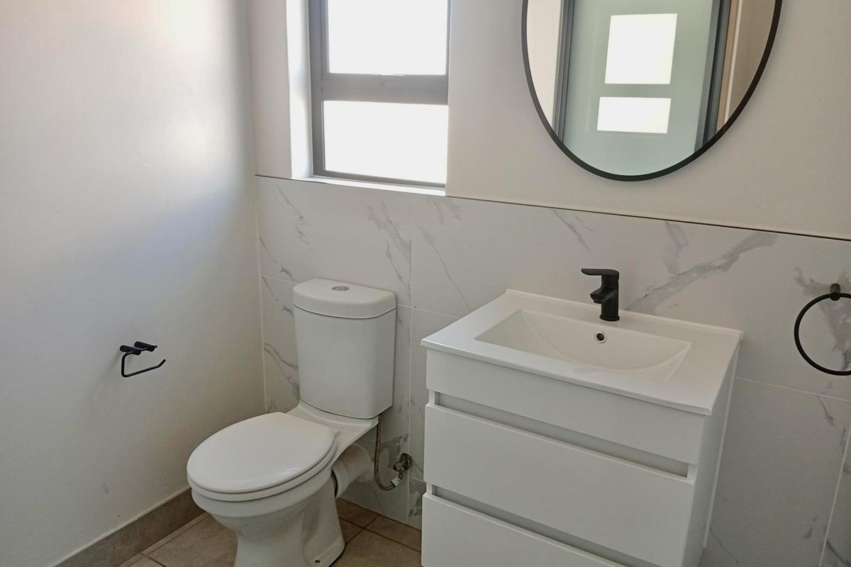 Modern bathroom featuring a sleek vanity cabinet with a black mixer tap, marble-look wall tiling, and a contemporary round mirror.
