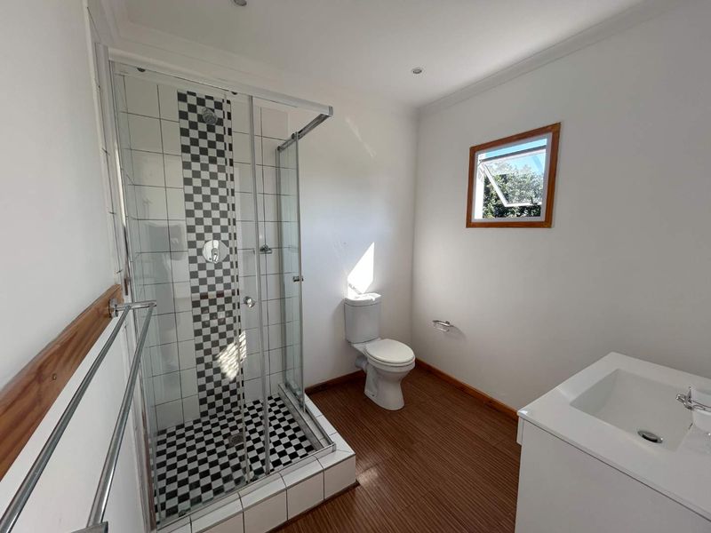 A clean and functional bathroom featuring a glass-enclosed shower with decorative checkered tiling, a white toilet, and a modern vanity basin.