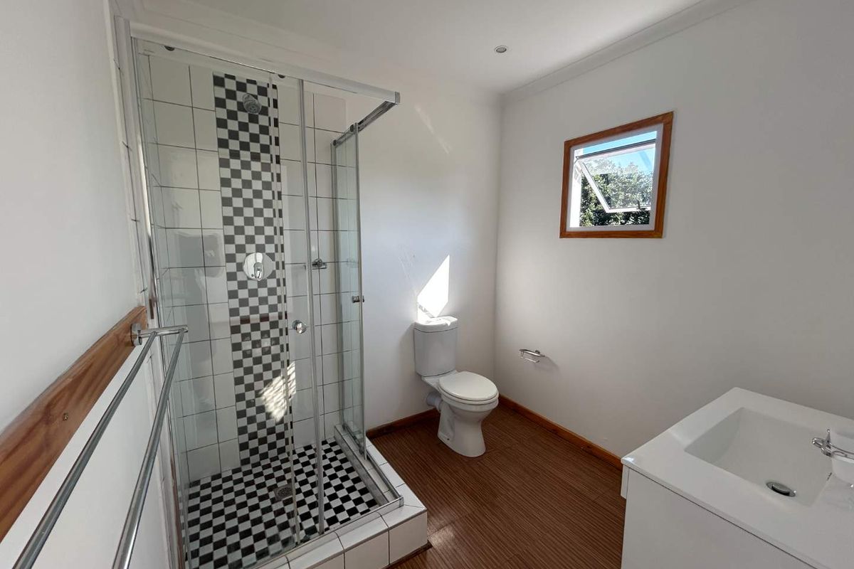 A clean and functional bathroom featuring a glass-enclosed shower with decorative checkered tiling, a white toilet, and a modern vanity basin.