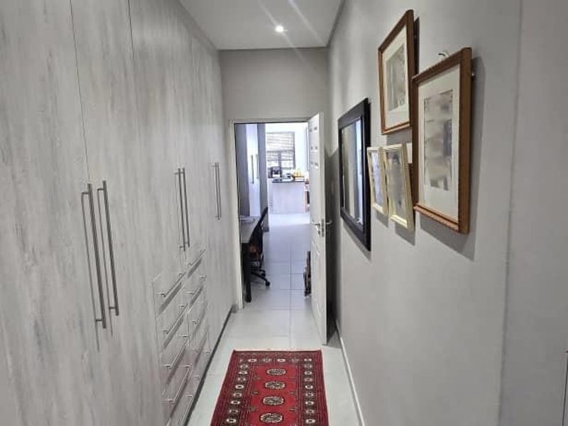 A well-lit hallway featuring extensive built-in cabinetry with modern handles and neutral tiled flooring, leading through to an adjacent room.