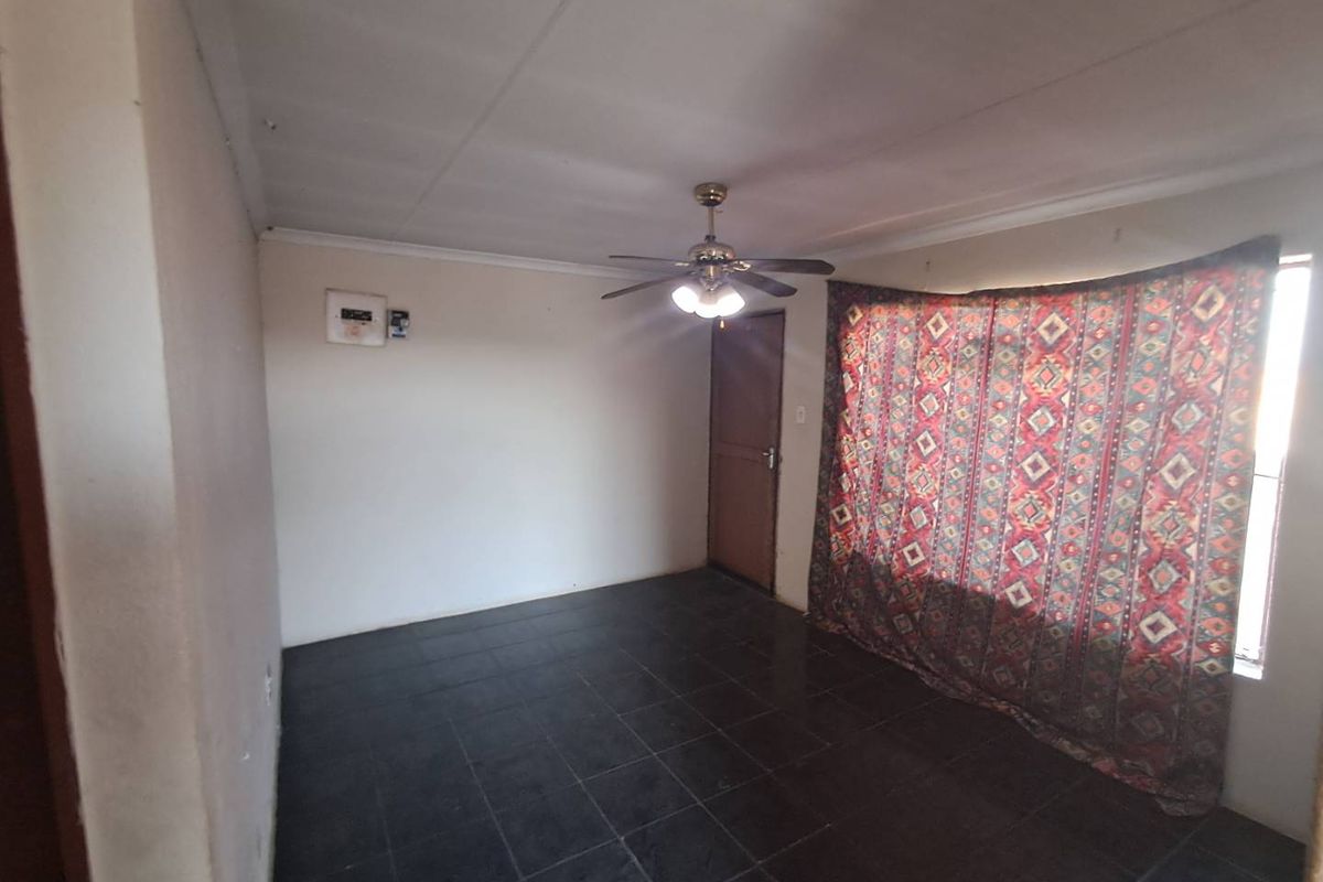 An empty living room featuring dark tiled flooring, a ceiling fan with integrated lighting, and a single door entrance.