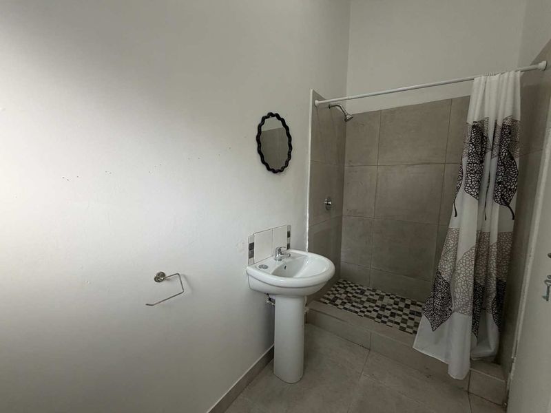A functional bathroom featuring a pedestal basin, a tiled shower enclosure, and neutral floor tiling.