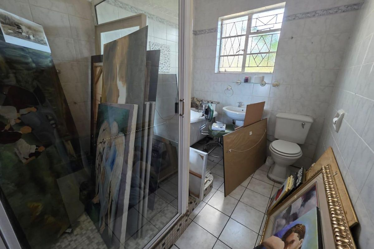 A dated bathroom featuring a glass-enclosed shower, pedestal basin, and toilet, currently used for storage. Requires renovation to modernize the space.