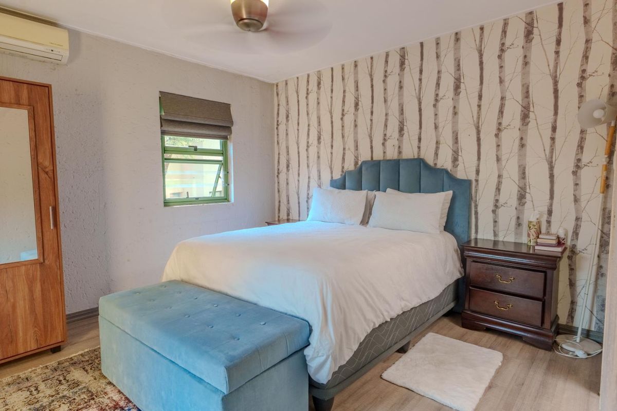 A bedroom featuring wood-look flooring, a ceiling fan, and a wall-mounted air conditioning unit.