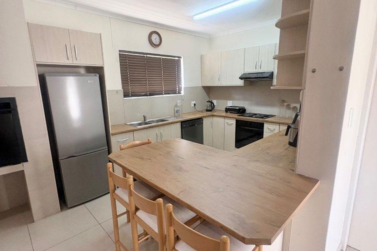 A functional kitchen featuring light wood-toned cabinetry, a breakfast bar, tiled flooring, and integrated appliances including a hob and extractor fan.