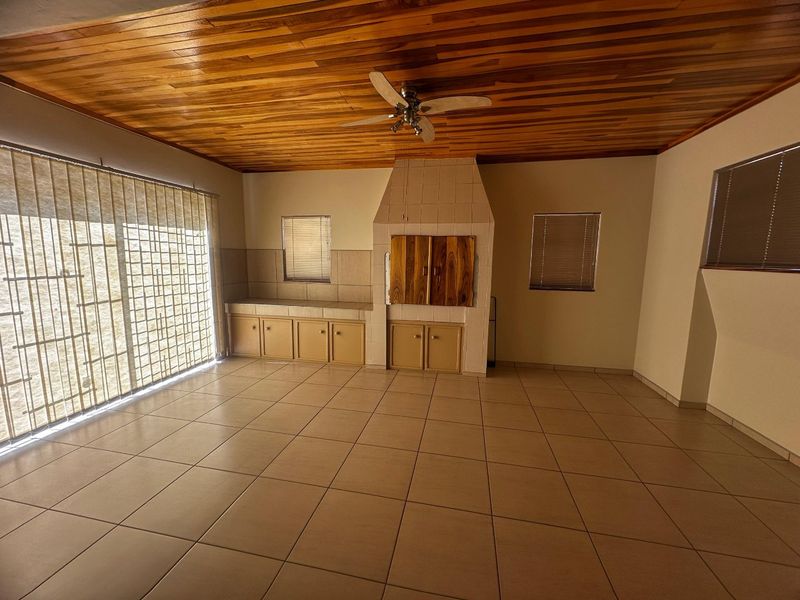 Spacious living area featuring a timber-clad ceiling, tiled flooring, and a built-in braai with integrated cabinetry.