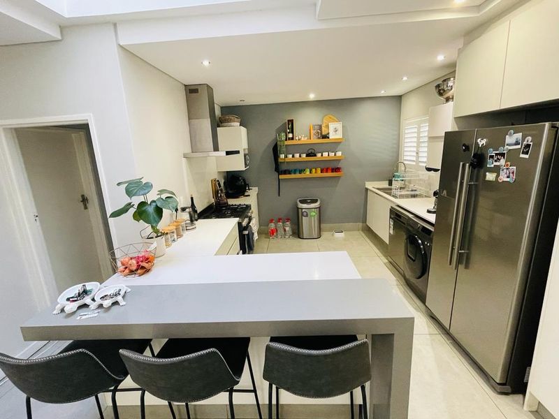 Modern kitchen featuring a breakfast bar, quartz countertops, built-in oven, extractor fan, and sleek cabinetry with recessed lighting.