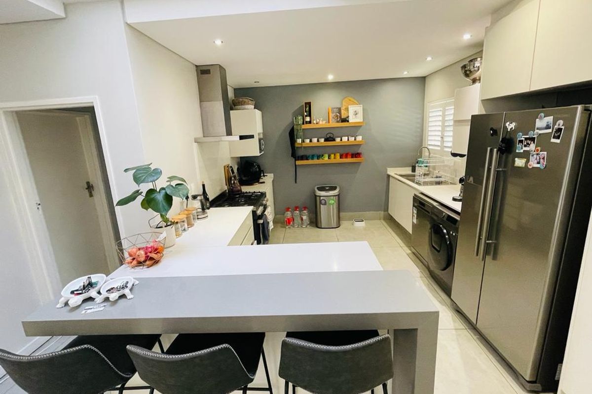 Modern kitchen featuring a breakfast bar, quartz countertops, built-in oven, extractor fan, and sleek cabinetry with recessed lighting.