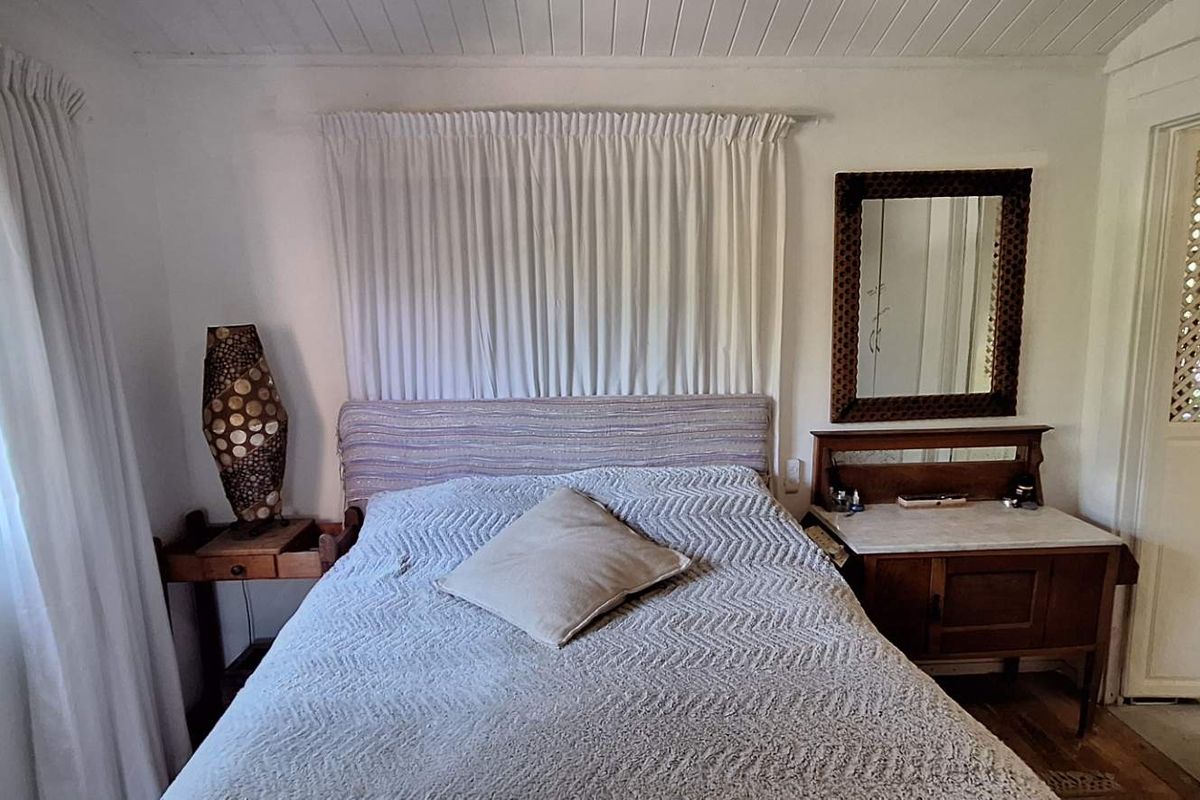 A cozy bedroom featuring a timber-framed window with security bars, tongue and groove ceiling, and a classic panelled door leading to an adjacent space.