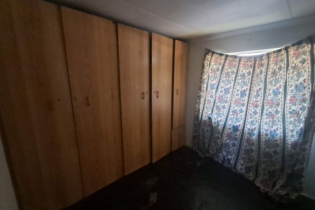 A bedroom featuring extensive built-in wooden cabinetry and a window with curtaining, offering functional storage space.