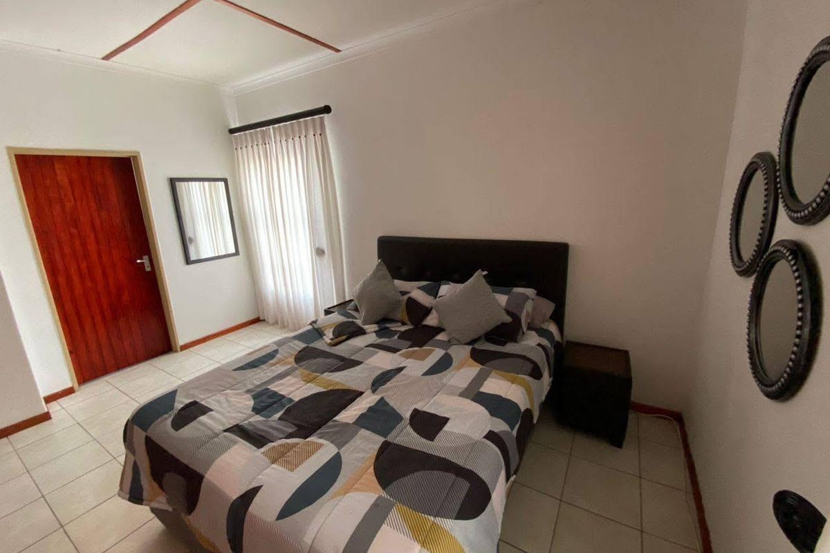 A bedroom featuring tiled flooring, a wooden door, and a window with curtains.