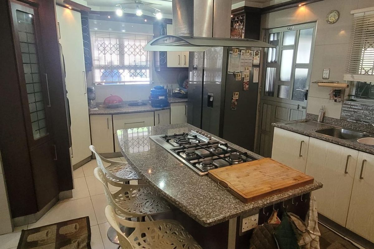 A functional kitchen featuring a central island with a gas hob, granite countertops, ample cabinetry, and a stainless steel extractor fan.