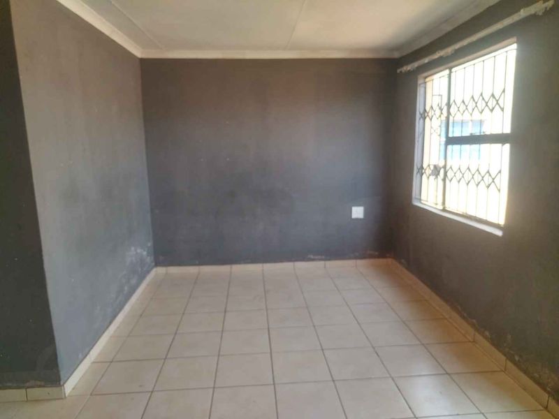 An empty bedroom featuring tiled flooring and security burglar bars on the window, requiring cosmetic attention to the walls.