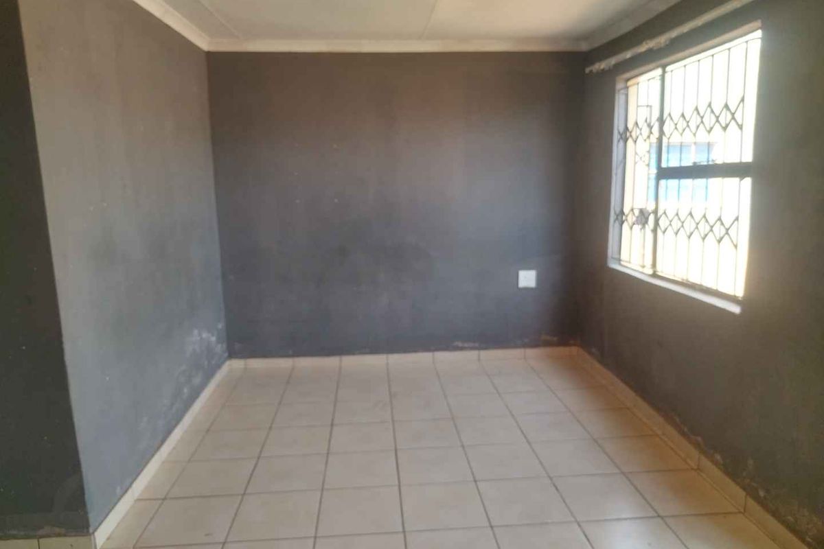 An empty bedroom featuring tiled flooring and security burglar bars on the window, requiring cosmetic attention to the walls.