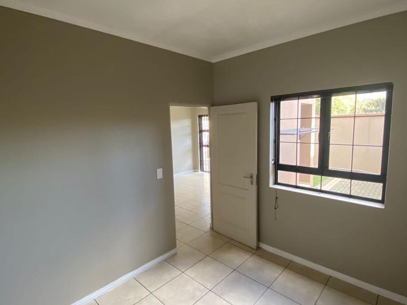 A clean, empty bedroom featuring neutral wall tones, tiled flooring, and an aluminium window with security bars, offering a bright and versatile living space.