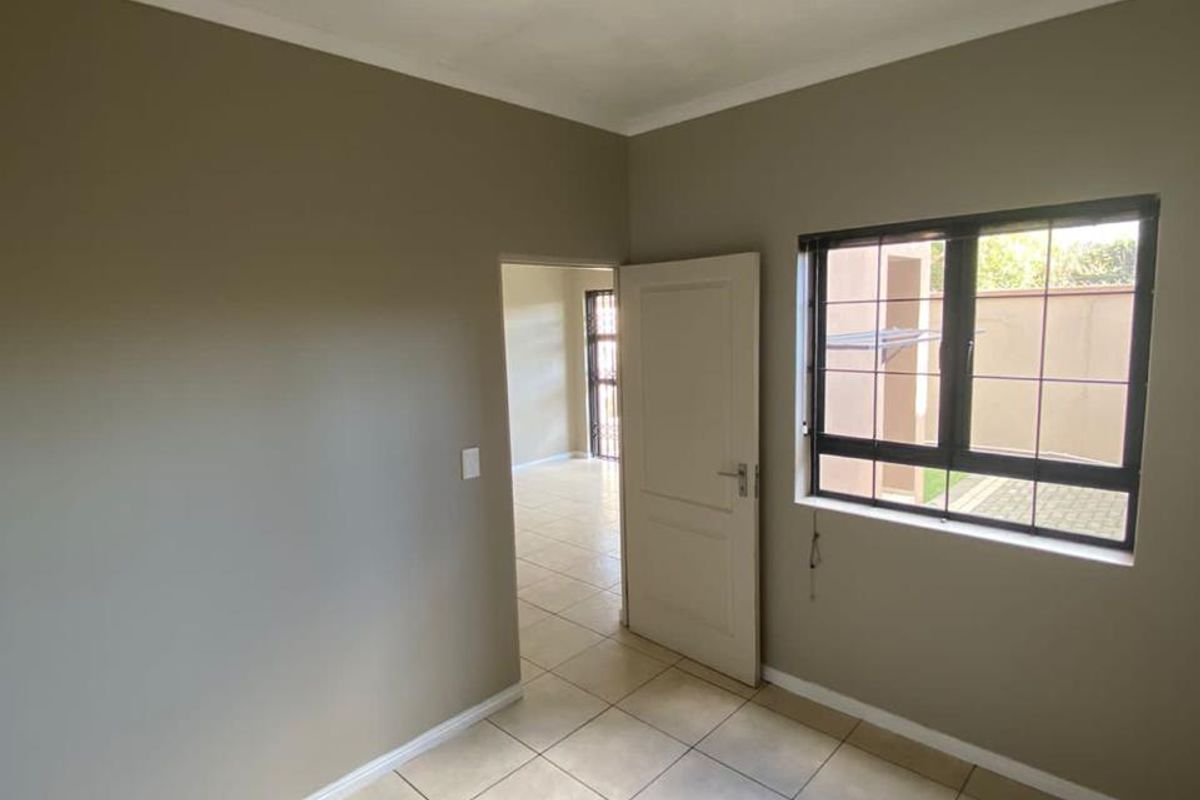 A clean, empty bedroom featuring neutral wall tones, tiled flooring, and an aluminium window with security bars, offering a bright and versatile living space.