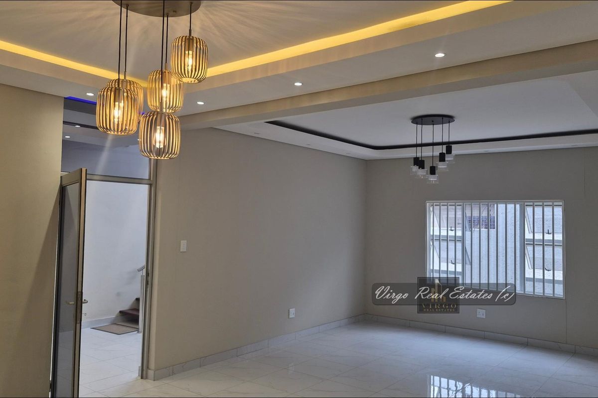 A bright, modern living area featuring tiled floors, recessed cove lighting, and contemporary pendant light fixtures, presenting a clean and well-maintained space.