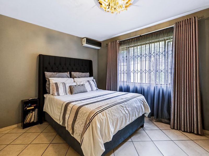 A well-maintained bedroom featuring tiled flooring, a split-system air conditioner, and a large window fitted with a security gate.