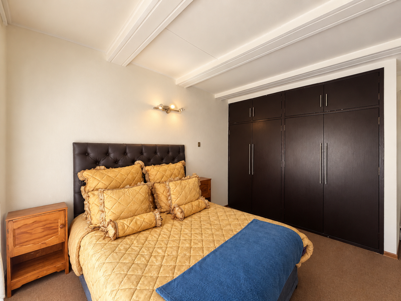 A well-maintained bedroom featuring dark built-in cupboards, exposed ceiling beams, and a wall-mounted light fixture.