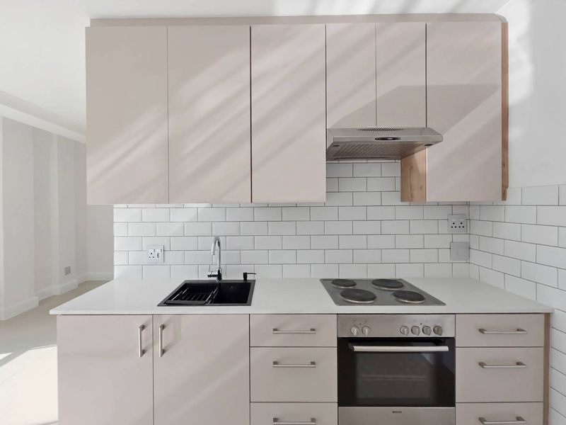 Modern kitchen featuring sleek neutral cabinetry, subway tile backsplash, integrated electric hob, oven, extractor fan, and a contemporary undermount sink.
