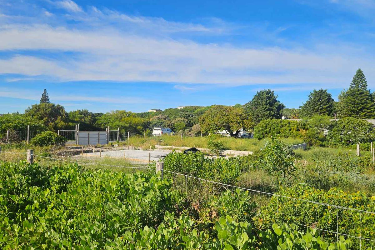 A vacant residential plot featuring a prepared concrete foundation slab, enclosed by wire mesh fencing and surrounded by established coastal vegetation.