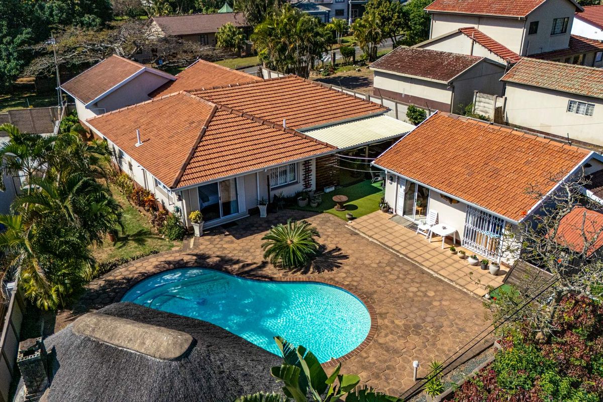 Aerial view of the property featuring a swimming pool, paved patio area, and multiple structures with tiled and thatched roofing.