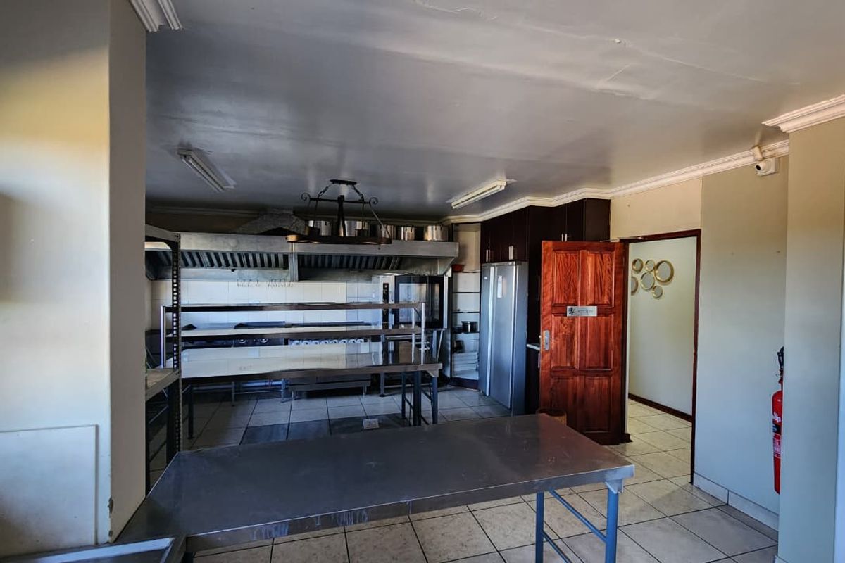 Commercial-style kitchen featuring stainless steel prep tables, industrial extractor hood, tiled flooring, and direct access to an adjacent hallway.