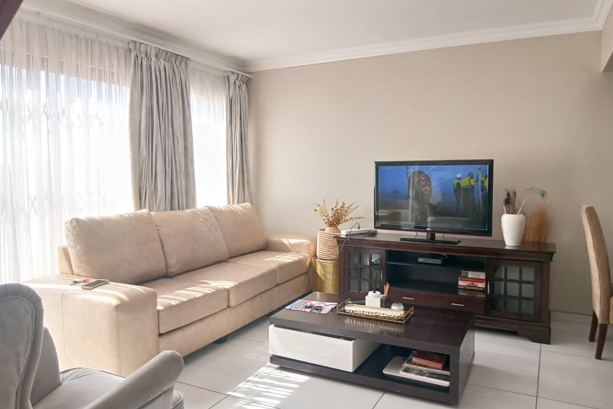 A bright and well-maintained living room featuring neutral tiled flooring, coved ceilings, and large sliding glass doors that provide ample natural light.