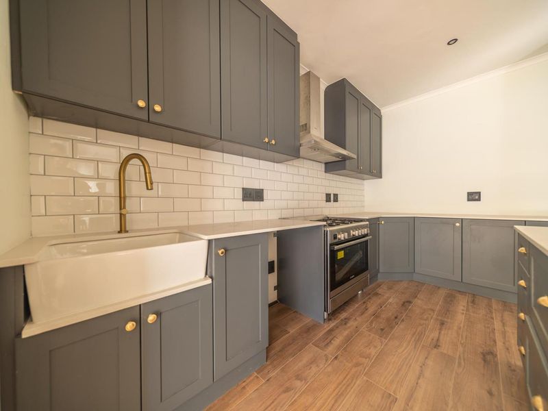 Modern kitchen featuring grey shaker-style cabinetry, subway tile backsplash, farmhouse sink with brass faucet, and stainless steel gas range.