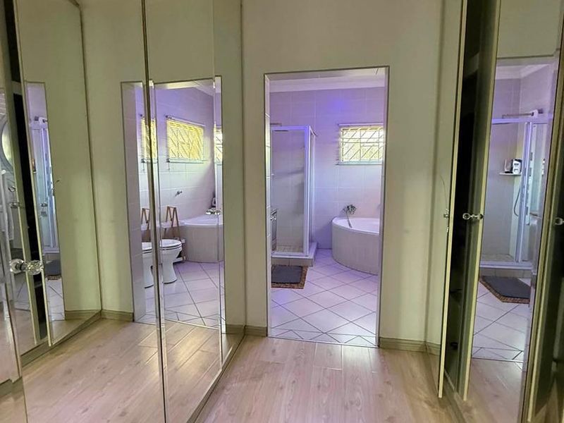 A hallway featuring extensive mirrored built-in cupboards with laminate flooring, leading directly into a tiled bathroom equipped with a corner bathtub and shower.