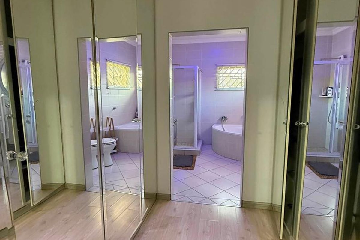 A hallway featuring extensive mirrored built-in cupboards with laminate flooring, leading directly into a tiled bathroom equipped with a corner bathtub and shower.