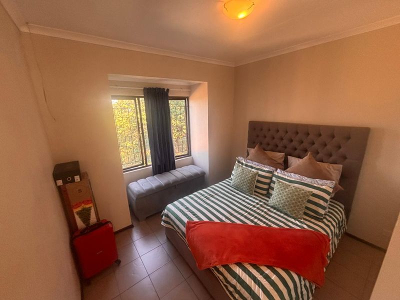 A cozy bedroom featuring tiled flooring, a window with security bars, and a central ceiling light fixture.
