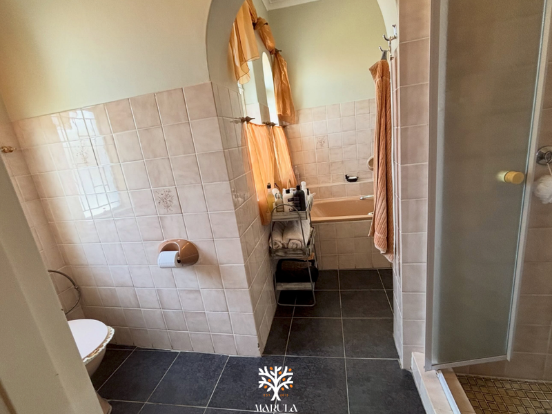 A functional bathroom featuring a built-in bathtub, separate shower enclosure, and neutral wall tiling with dark floor tiles.