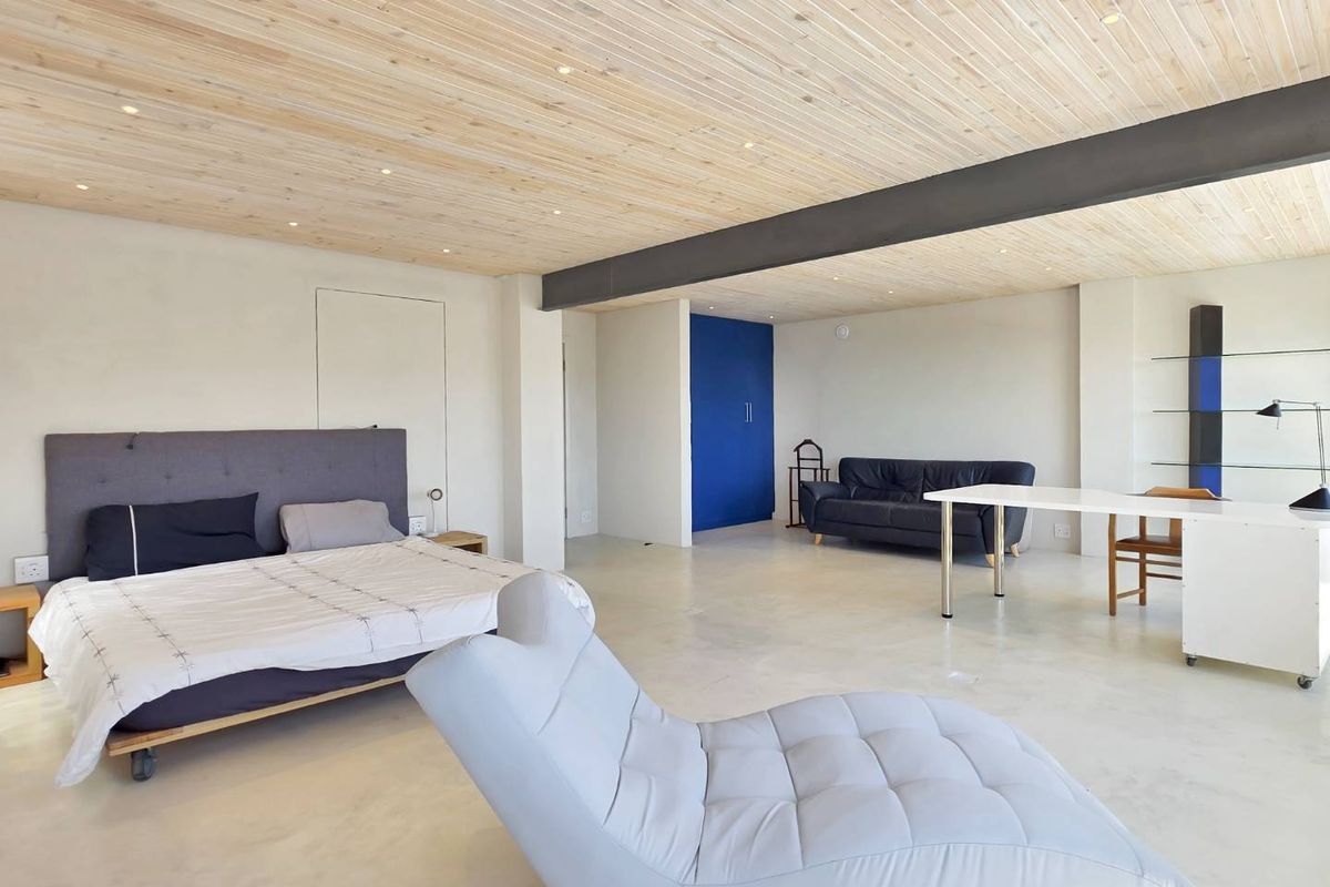 Spacious bedroom featuring a timber-clad ceiling, exposed steel beam, and polished concrete flooring with integrated storage and recessed lighting.