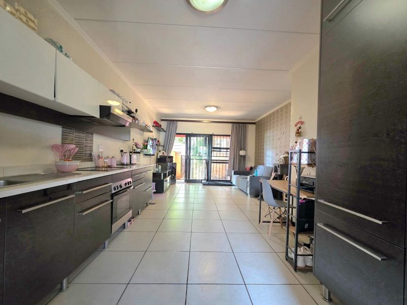 Open-plan living area featuring a modern kitchen with dark cabinetry, tiled flooring, and direct access to an outdoor patio through a security gate.