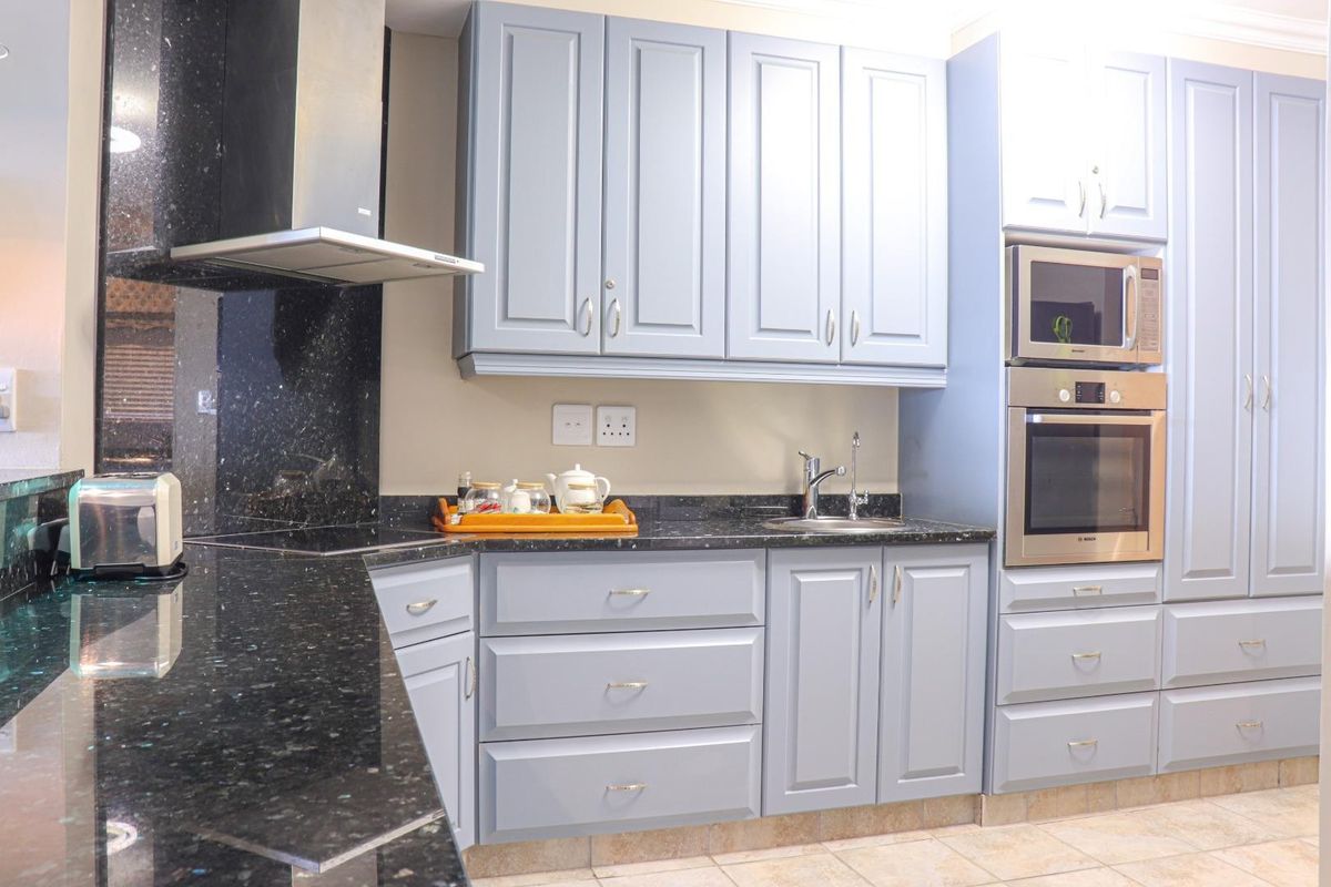 Modern kitchen featuring light blue cabinetry, dark granite countertops, stainless steel extractor fan, built-in oven, and microwave with tiled flooring.
