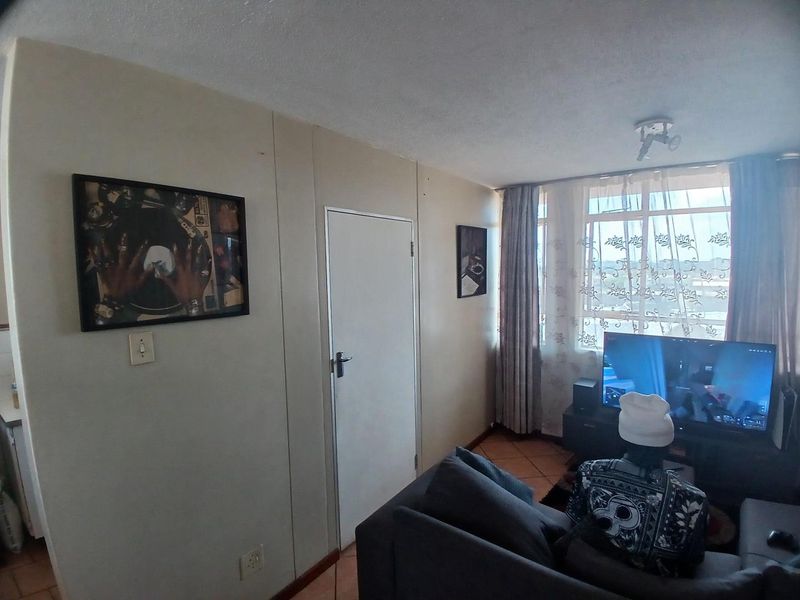 A living room area featuring tiled flooring, a large window allowing natural light, and a standard internal door.