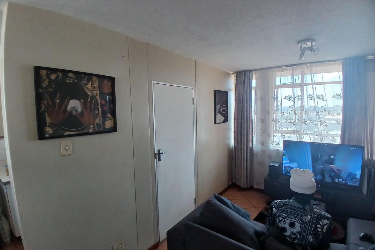 A living room area featuring tiled flooring, a large window allowing natural light, and a standard internal door.