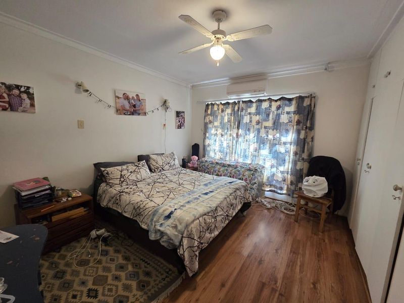 A functional bedroom featuring laminate flooring, a ceiling fan, and a wall-mounted split-system air conditioner for climate control.