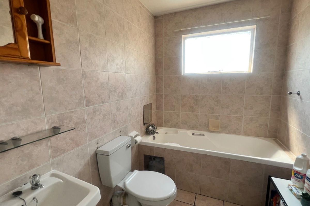 A functional bathroom featuring a built-in bathtub, ceramic wall tiling, a standard toilet, and a wall-mounted basin.