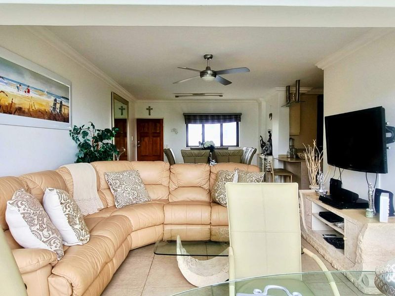 Spacious open-plan living and dining area featuring tiled flooring, a ceiling fan, and a functional kitchen breakfast counter.