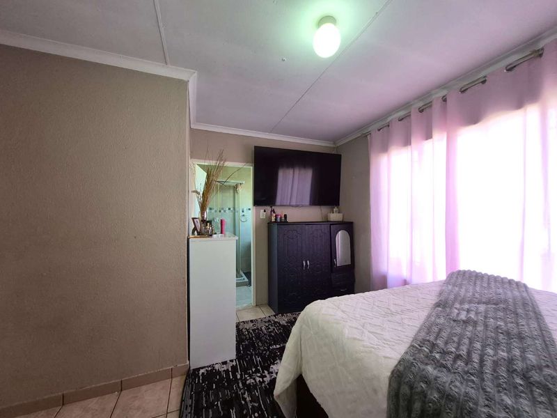 A bedroom featuring tiled flooring and direct access to an en-suite bathroom, with neutral wall tones and natural light from the window.