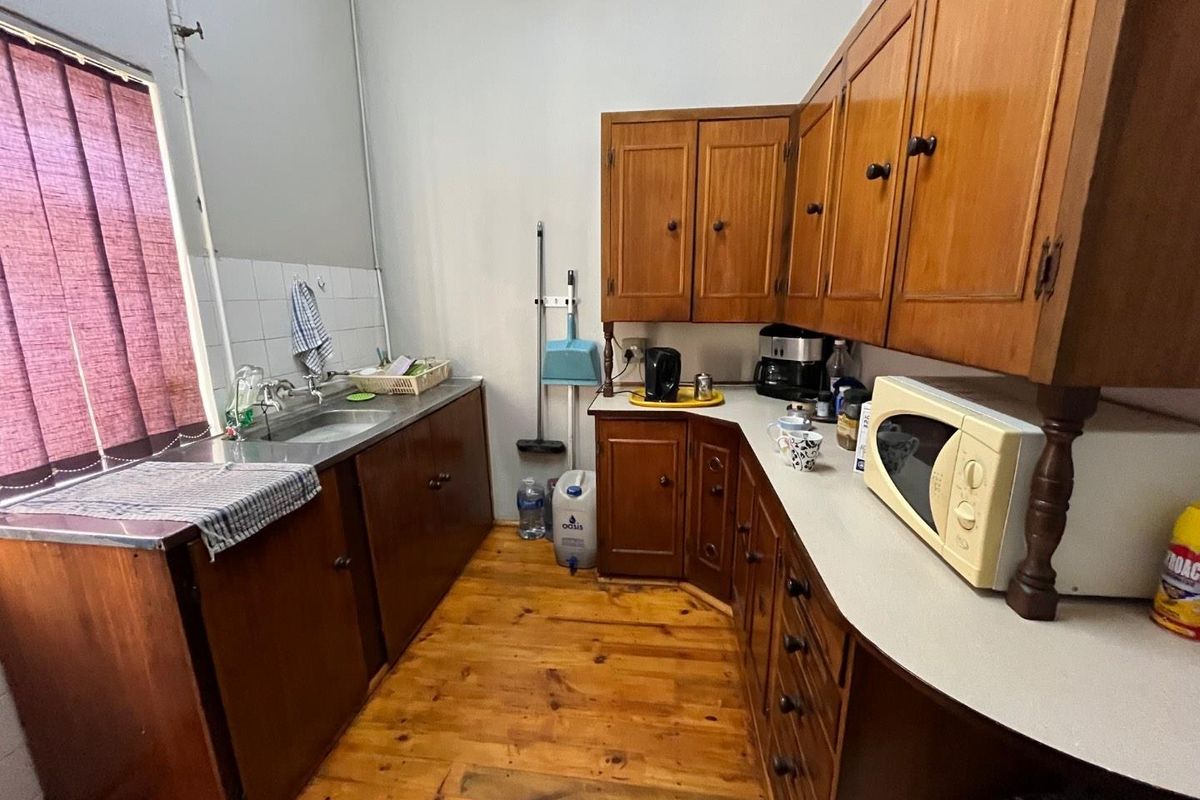 A functional office kitchenette featuring traditional wooden cabinetry, laminate countertops, a stainless steel sink, and polished timber flooring.