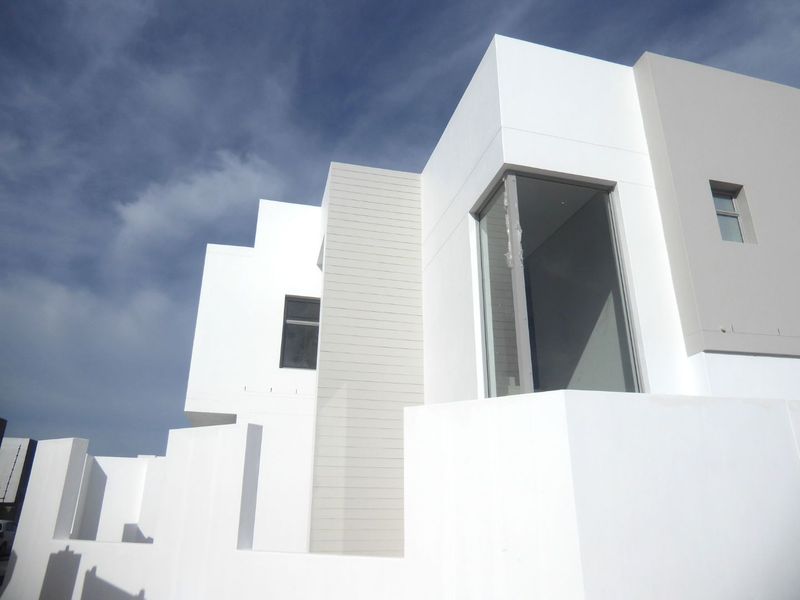 A modern architectural exterior featuring clean white lines, horizontal cladding accents, and large aluminum-framed windows under a clear blue sky.