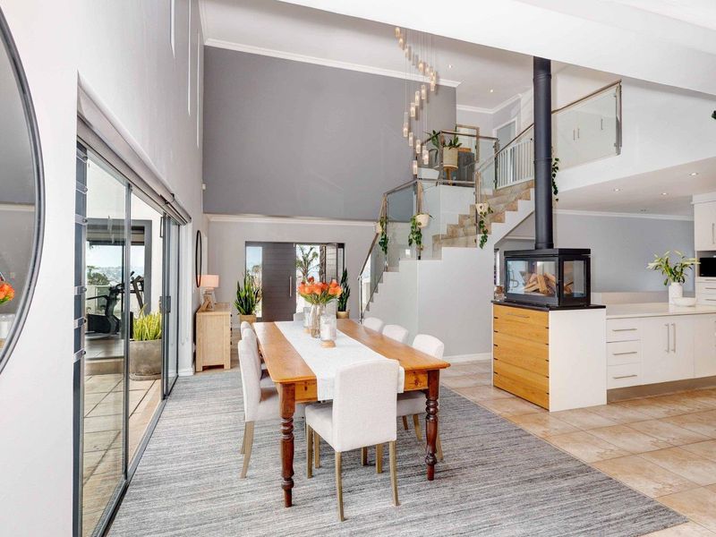 Spacious open-plan living and dining area featuring a modern freestanding fireplace, high ceilings, and a striking glass balustrade staircase leading to the upper level.