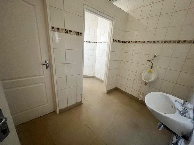 A functional commercial-style bathroom featuring tiled walls and floors, equipped with a wall-mounted urinal and a washbasin.